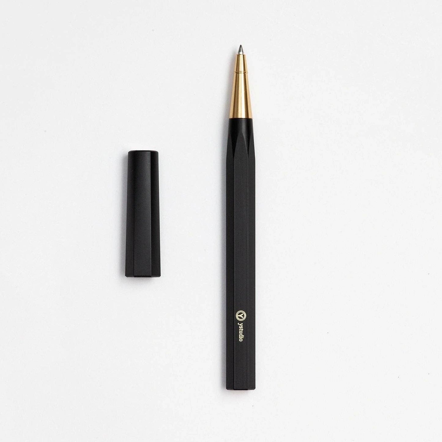 Der ENTREPÔT - YSTUDIO Harz-Rollerball-Stift (Schwarz) verfügt über eine goldene Spitze, eine schwarze Kappe auf der linken Seite und ein Markenlogo in der Nähe der Basis, alles vor einem weißen Hintergrund, um sein Schreibritual hervorzuheben.