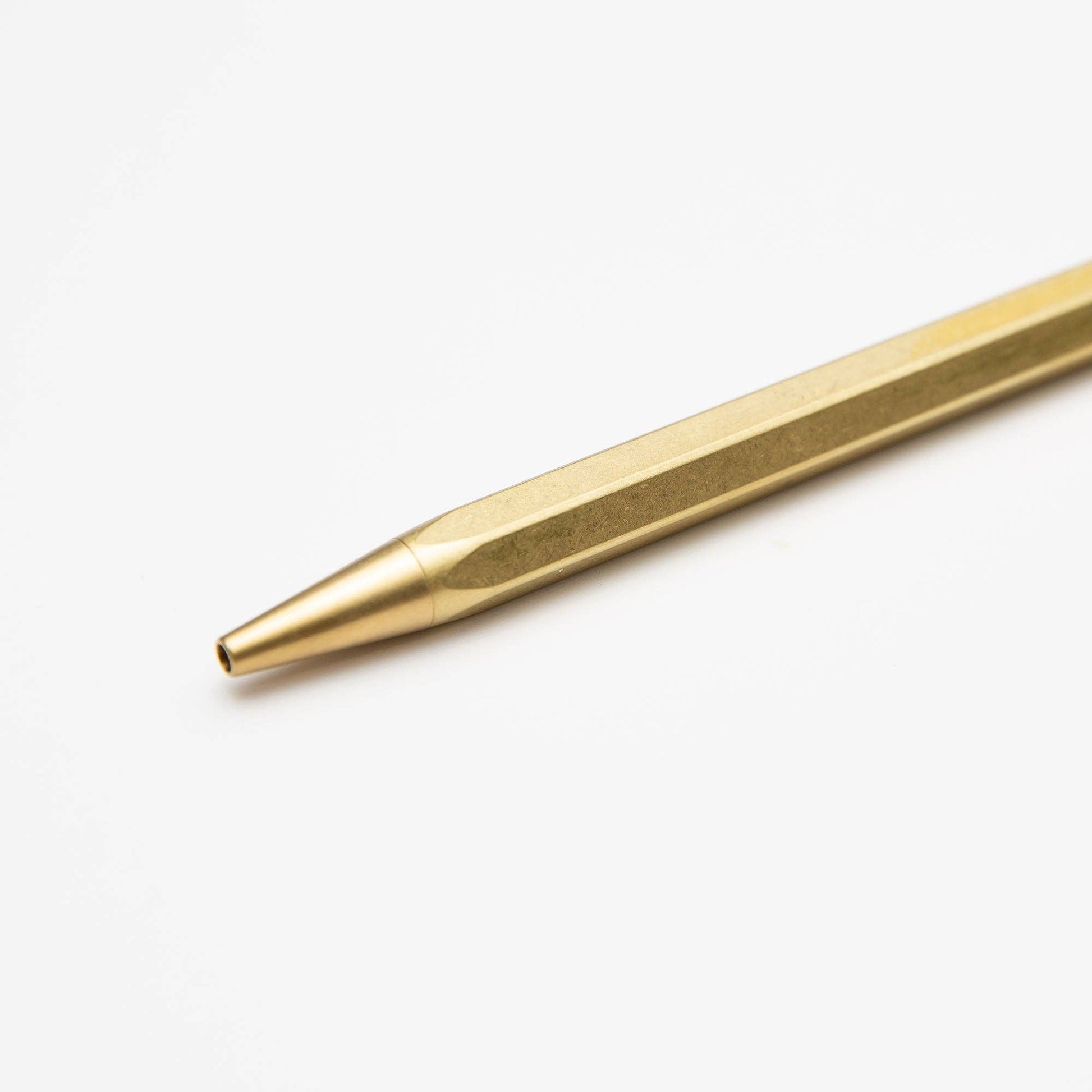 Eine Nahaufnahme der ENTREPÔT - YSTUDIO Klassischer Revolve Kugelschreiber Feder (Messing) mit schlankem, kantigem Korpus und langlebiger Federkappenstruktur, diagonal auf weißem Hintergrund platziert, mit der Spitze nach links unten zeigend.