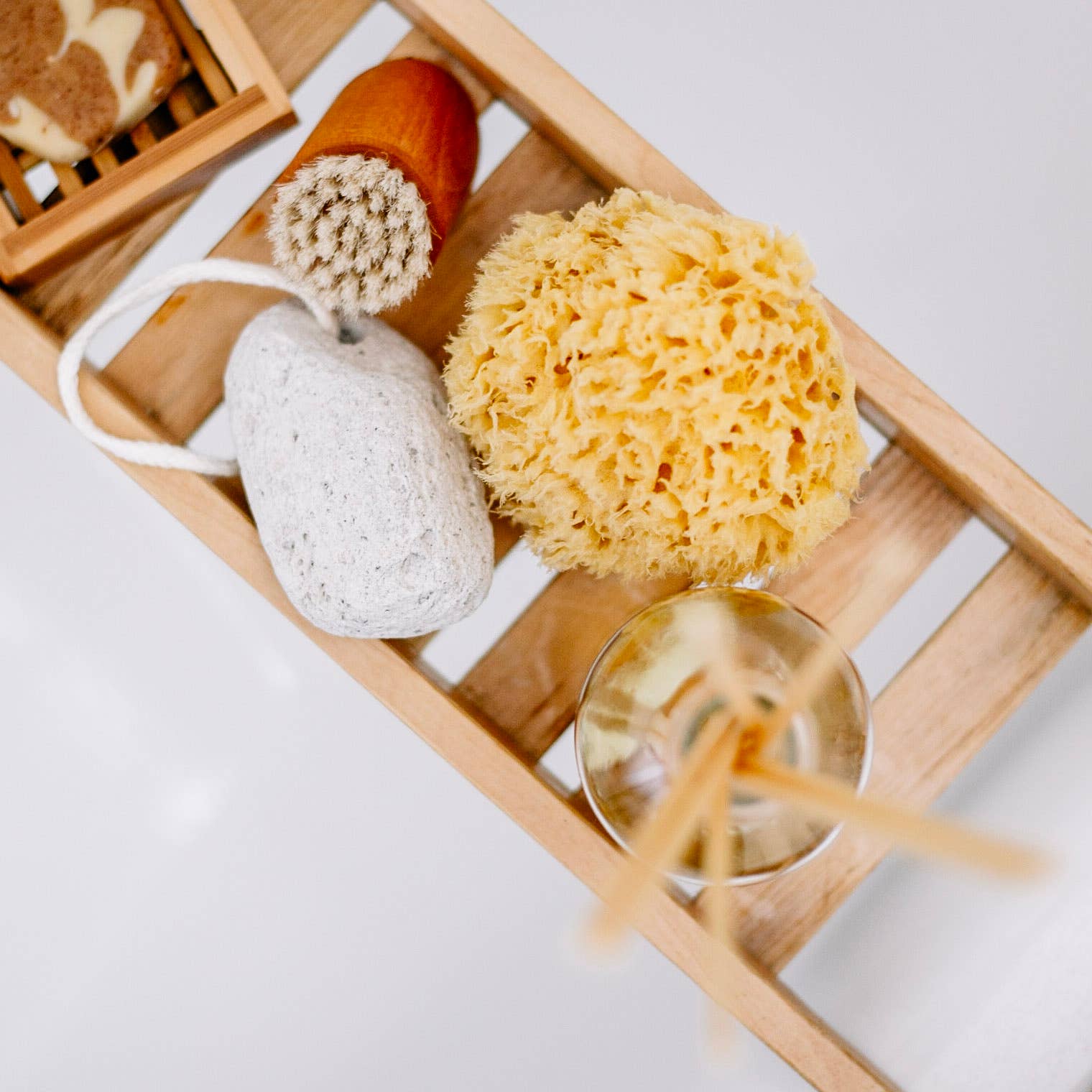 Eine hölzerne Badeschale enthält einen Croll & Denecke nachhaltigen Naturschwamm, einen Bimsstein mit Schnur, eine Körperbürste, Schilfrohrdüsen in einem Gefäß und eine Seifenschale mit Naturseife - alles von oben betrachtet.