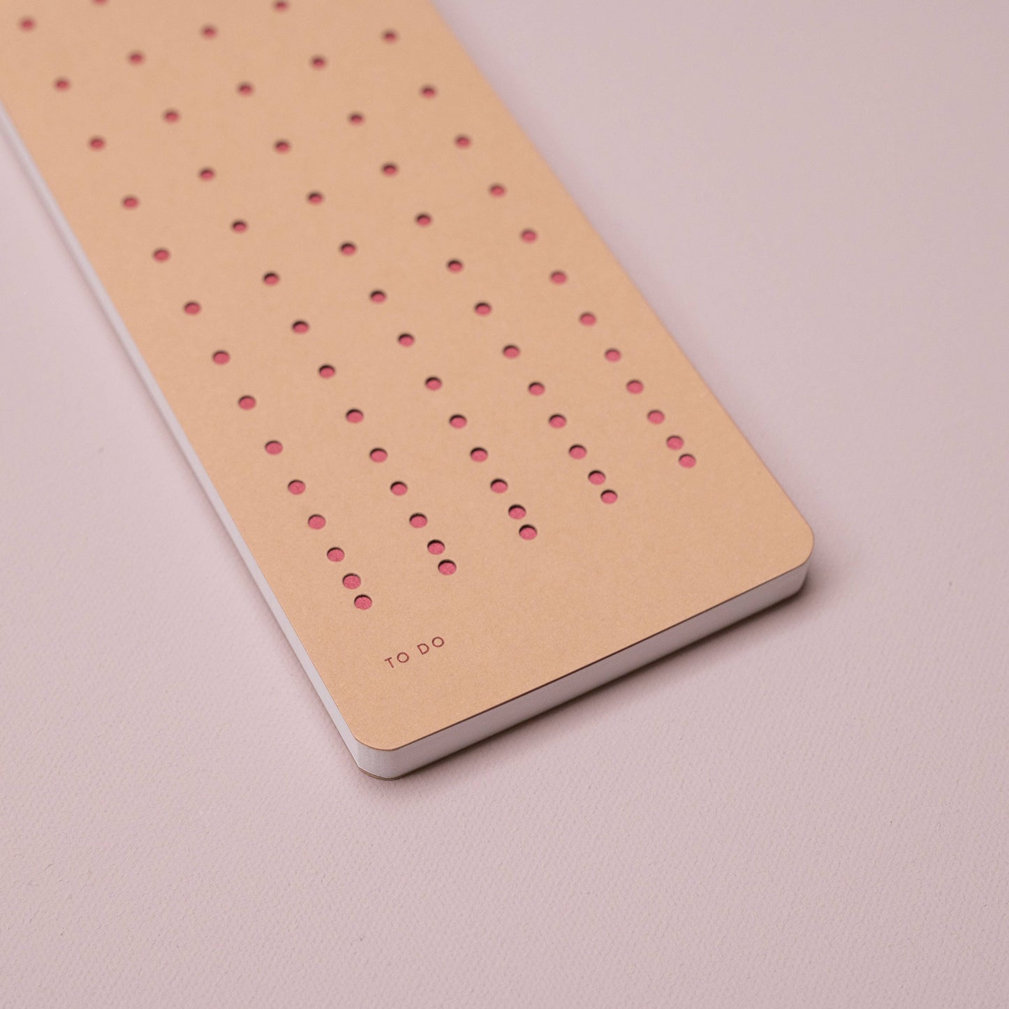 Der Tinne Mia - Aufgabenliste - Nougat ist ein minimalistischer Notizblock von Tinne Mia aus FSC-zertifiziertem Papier mit gleichmäßiger Lochung und dem Schriftzug "TO DO" in kleiner Schrift unten links auf hellrosa Oberfläche.