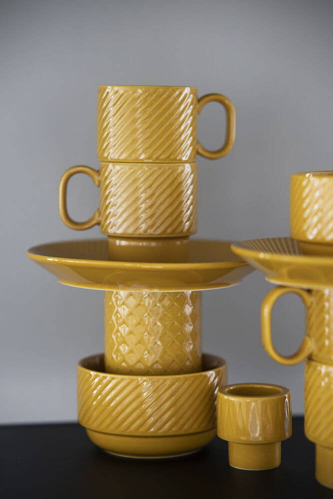 Ein Set senfgelber Kaffeebecher (2-teilig) von Sagaform GmbH Coffee & More ist auf einem grauen Hintergrund mit anderem Keramikgeschirr arrangiert abgebildet.
