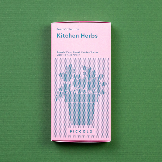 Eine rosafarbene Piccolo Seeds - Küchenkräuter-Packung von Piccolo Seeds mit einer gepixelten Topfkräuter-Illustration und der Aufschrift "gentechnikfrei" steht auf einem grünen Hintergrund. Enthält Samen für Kerbel, Schnittlauch und Petersilie.