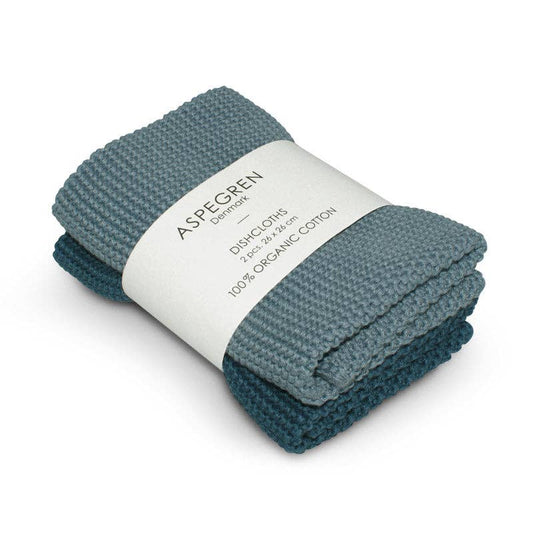 Zwei blaue, gestrickte Aspegren Denmark Spültücher aus 100 % Bio-Baumwolle sind zusammengerollt und mit einem Etikett mit der Aufschrift „ASPEGREN Denmark DISHCLOTHS 25 x 25 cm, 100 % ORGANIC COTTON“ umwickelt.