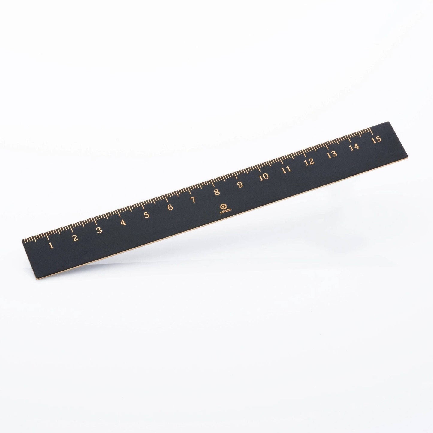 Ein 15 cm langes schwarzes ENTREPÔT - YSTUDIO Klassischer Reflect Lineal mit goldenen Markierungen liegt diagonal auf weißem Grund - ein elegantes Designer-Büroaccessoire und hochwertiges schwarzes Messing Lineal für Ihren Arbeitsbereich.