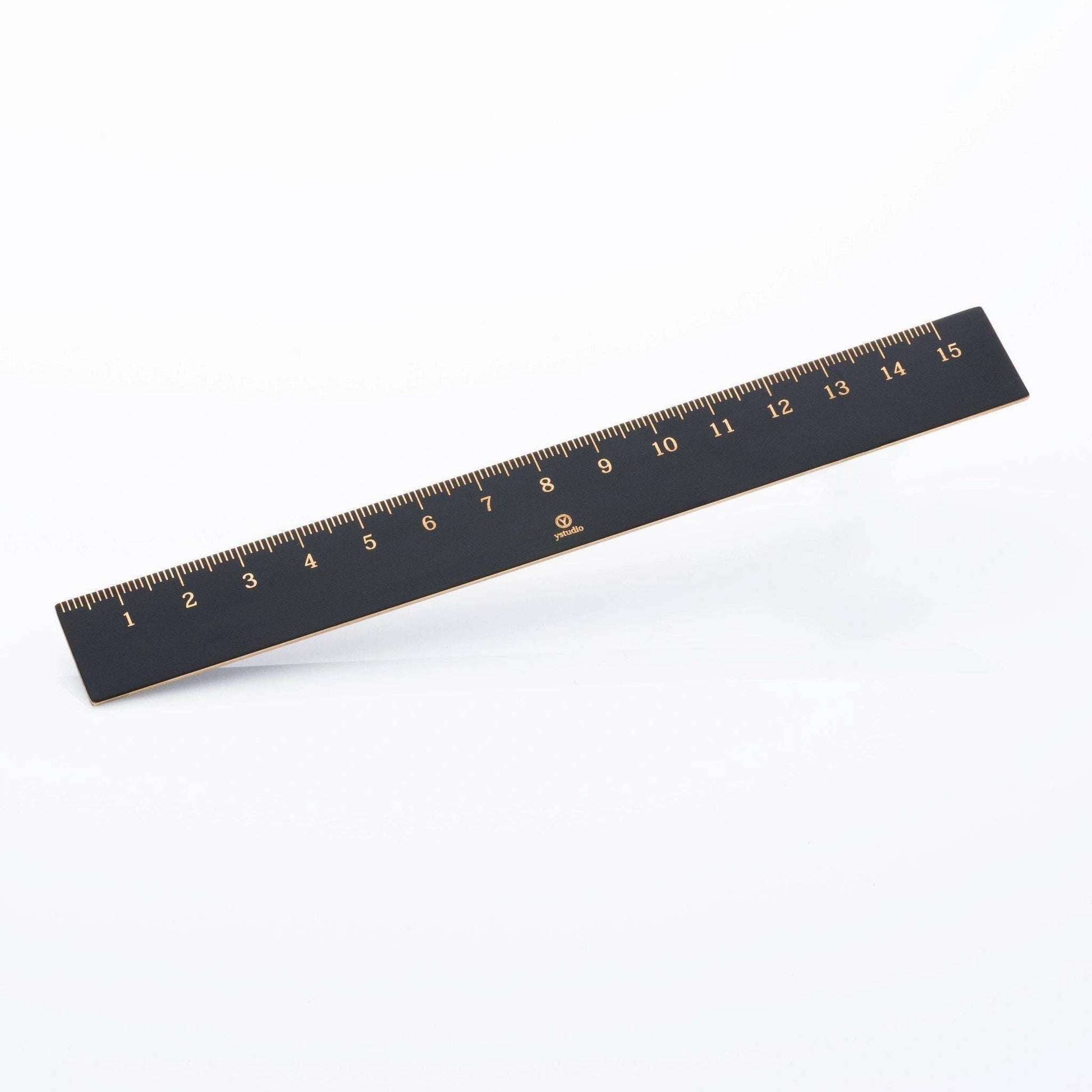 Ein 15 cm langes schwarzes ENTREPÔT - YSTUDIO Klassischer Reflect Lineal mit goldenen Markierungen liegt diagonal auf weißem Grund - ein elegantes Designer-Büroaccessoire und hochwertiges schwarzes Messing Lineal für Ihren Arbeitsbereich.