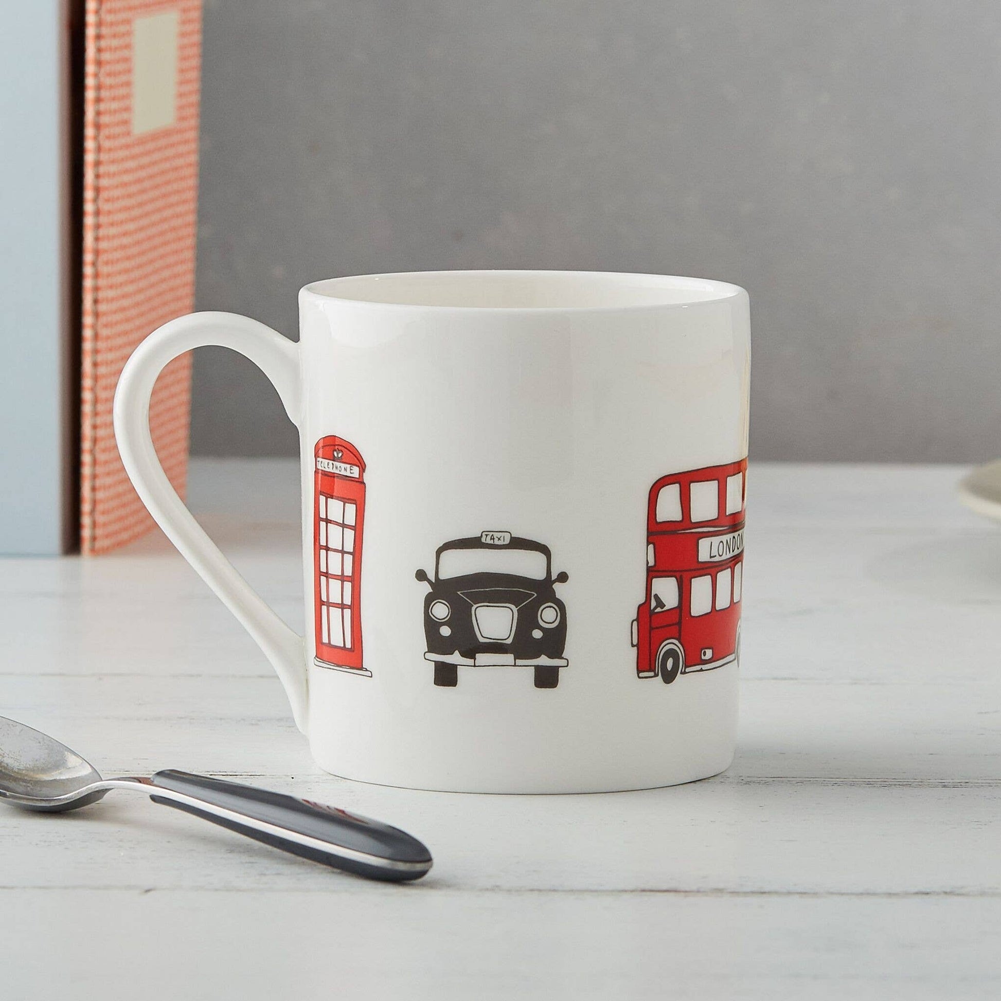 Der Victoria Eggs - London Skyline Becher von Victoria Eggs ist ein Becher aus feinem Knochenporzellan mit Abbildungen einer roten britischen Telefonzelle, eines schwarzen Taxis und eines roten Doppeldeckerbusses – ein bezauberndes britisches Souvenir für jeden Fan.