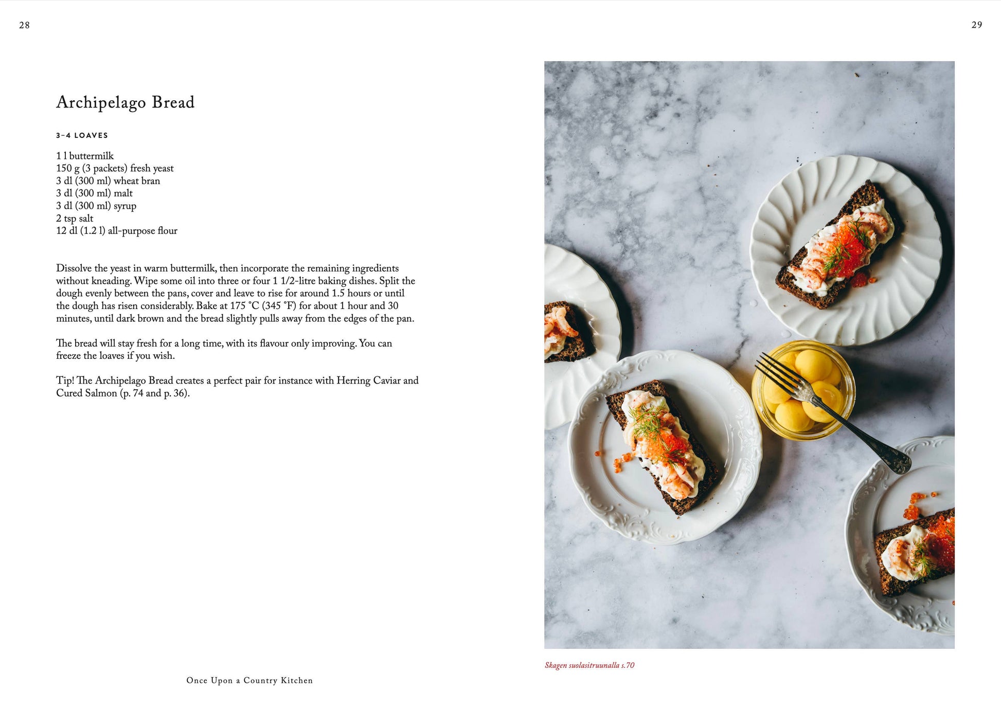 Eine Seite aus „Es war einmal eine Landhausküche“ von Cozy Publishing zeigt drei belegte Brötchen mit cremigem Aufstrich, geräuchertem Lachs und Rogen neben einer Schale mit Zitronen auf weißem Marmor und hebt die reinen Zutaten hervor.