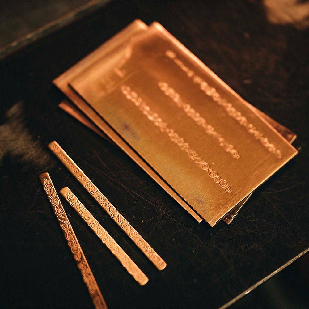 Der ENTREPÔT - YSTUDIO Klassische Renaissance KAZARI KANAGU ORCHID Tintenroller von ENTREPÔT zeigt auf einer dunklen Oberfläche aufwendige dekorative Metallmuster, die von der Metallgravurkunst und Kazari Kanagu inspiriert sind.