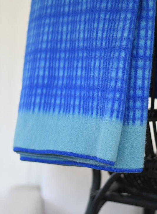 Die Darling Tagesdecke aus Lammwolle in Blau von Sofie Sjöström Design mit blau-kariertem Muster ist über einen schwarzen Stuhl drapiert.