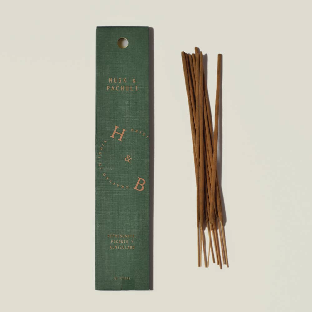 Eine grüne H&B-Weihrauchdose mit der Aufschrift "Natürlicher Moschus- und Patchouli-Weihrauch" steht neben braunen Räucherstäbchen. Die Schachtel hat einen goldenen kreisförmigen Text, eine Bodenbeschreibung und erinnert an Noten von natürlichem Moschus und Patchouli.