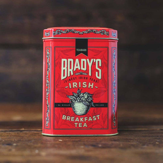 Eine rote Dose von Brady's Coffee Company - Bradys irischer Frühstückstee sitzt auf Holz und enthält 40 Teebeutel Schwarztee. Die Dose zeigt dekorative Muster und die Illustration eines Korbes mit Teeblättern.