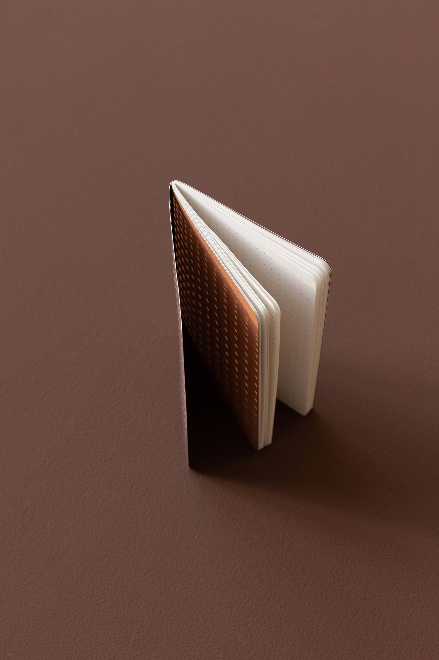 Das Tinne Mia - Bullet Journal A6 - Grid Burgunderrot von Tinne Mia steht aufrecht auf einer passenden burgunderroten Oberfläche. Sein kompaktes Format und die gerasterten, strukturierten FSC Mix-Seiten sind ideal für Notizen oder Skizzen.