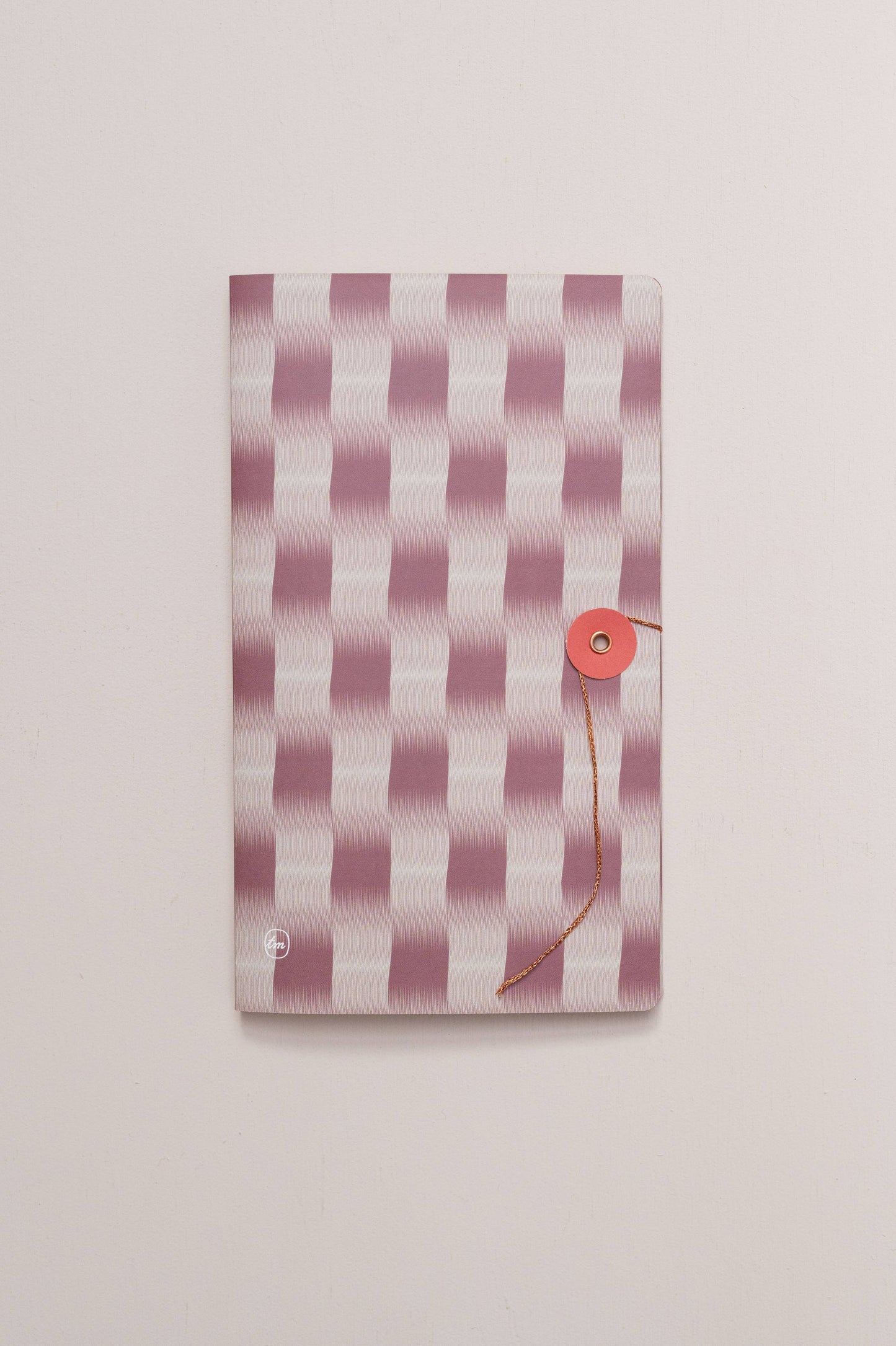 Das Tinne Mia Notizbuch mit japanischem Verschluss - Cinnamon zeichnet sich durch einen rosa-weiß gestreiften Einband mit rotem Rundverschluss aus, der vor einem schlichten, hellen Hintergrund steht.