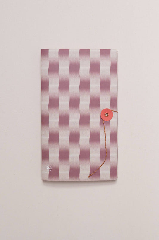 Das Tinne Mia Notizbuch mit japanischem Verschluss - Cinnamon zeichnet sich durch einen rosa-weiß gestreiften Einband mit rotem Rundverschluss aus, der vor einem schlichten, hellen Hintergrund steht.