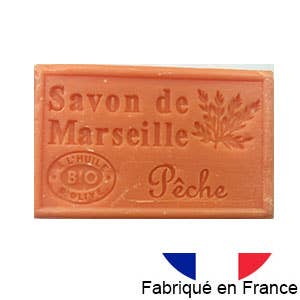 Die Dampa 1975 Marseiller Seife mit Bio-Olivenöl-Pfirsichduft ist ein rechteckiges orangefarbenes Stück Seife mit der Aufschrift „Savon de Marseille Pêche“ mit Zweigdesign, französischer Flagge und „Fabriqué en France“ – genießen Sie Pfirsichduft und französische Handwerkskunst.