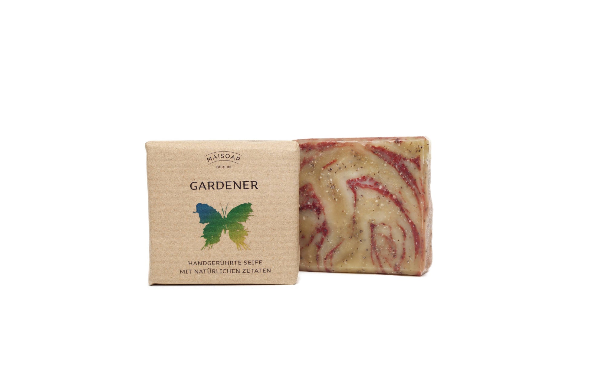 Ein Riegel maisoap berlin Gardener Seife mit roten und beigen Strudeln steht neben seiner braunen Papierverpackung mit der Aufschrift "GARDENER", die ein grün-gelber Schmetterling ziert - ein perfekter Leckerbissen für Gartenhände mit einer minzigen Duftnote.