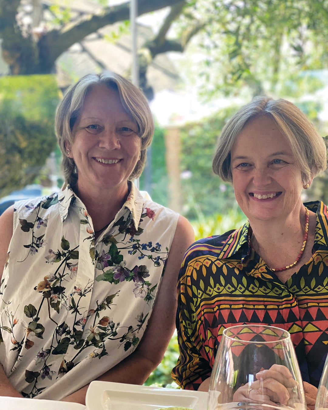 Zwei Frauen sitzen lächelnd im Grünen und besuchen die Königliche Gartenakademie MASTER CLASS "Gestalten Sie Ihren eigenen Garten - Gärten bis 3000 qm", die vom 24.-26.03.2026, 10:00-16:30 Uhr stattfindet.