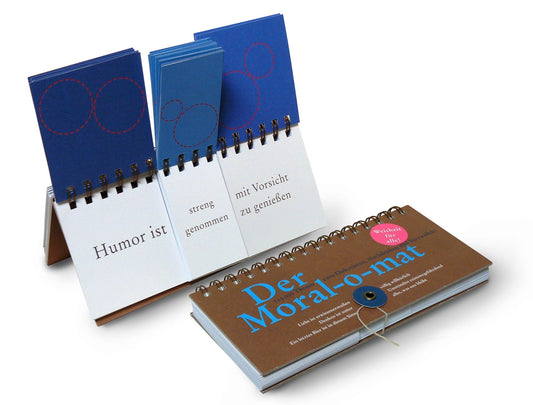 Ein spiralgebundenes Daumenkino mit dem Titel Der Moral-O-mat von Thesen zum Diskutieren, Nachdenken & Ver wird gezeigt, eines offen für deutsche Phrasen und eines geschlossen. Der braune Einband ist mit blauer und weißer Schrift und einem rosa Aufkleber versehen und lädt zu ethischen Diskussionen ein.