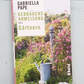 Buch - Gebrauchsanweisung fürs Gärtnern von Gabriella Pape liegt auf hellem Holz. Das Cover zeigt einen blühenden Garten mit Gießkanne und Tipps für den perfekten Rasen.