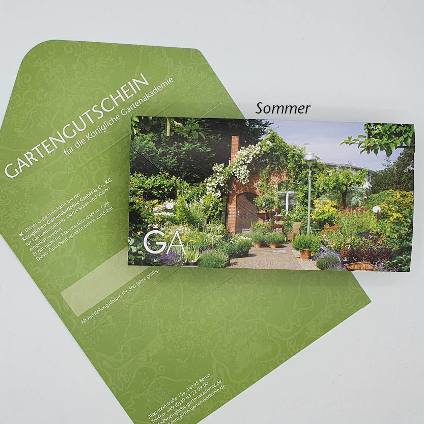 Ein grüner Gutschein für die Königliche Gartenakademie mit passendem Umschlag und botanischem Design der Königlichen Gartenakademie liegt neben einem farbenfrohen Sommerfoto mit üppigen Pflanzen und einer gemauerten Pergola.