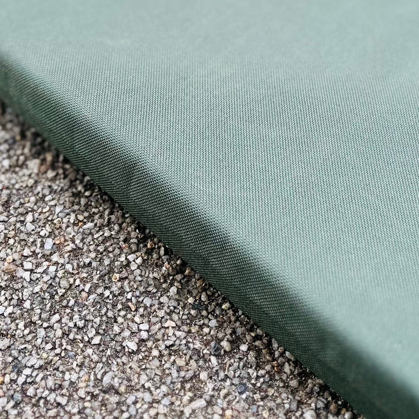 Eine Nahaufnahme des grünen Esschert Kniekissens von Eschert Design, dessen glatte Oberfläche im Kontrast zum rauen, gesprenkelten Beton steht, unterstreicht den weichen Schutz, den es bei der Gartenarbeit auf hartem Boden bietet.